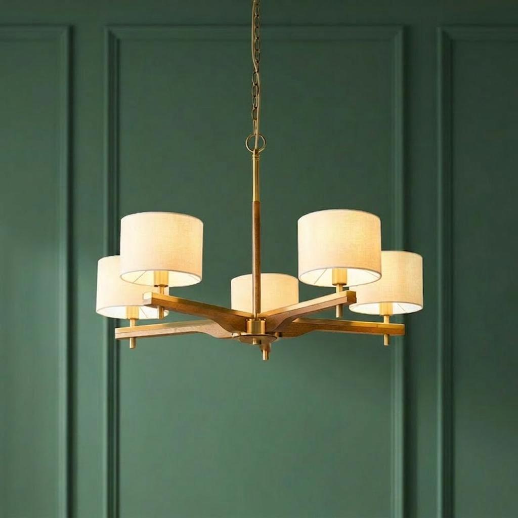 Heathcliff five-arm wood and brass pendant light with beige shades set against a dark green paneled wall.