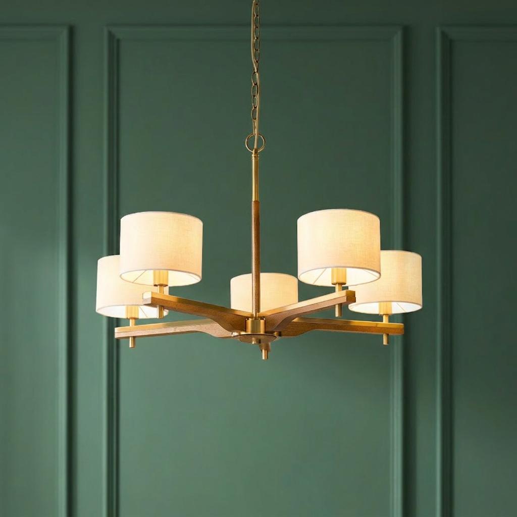 Heathcliff 5-arm wood and brass pendant light with drum shades against a green paneled wall.