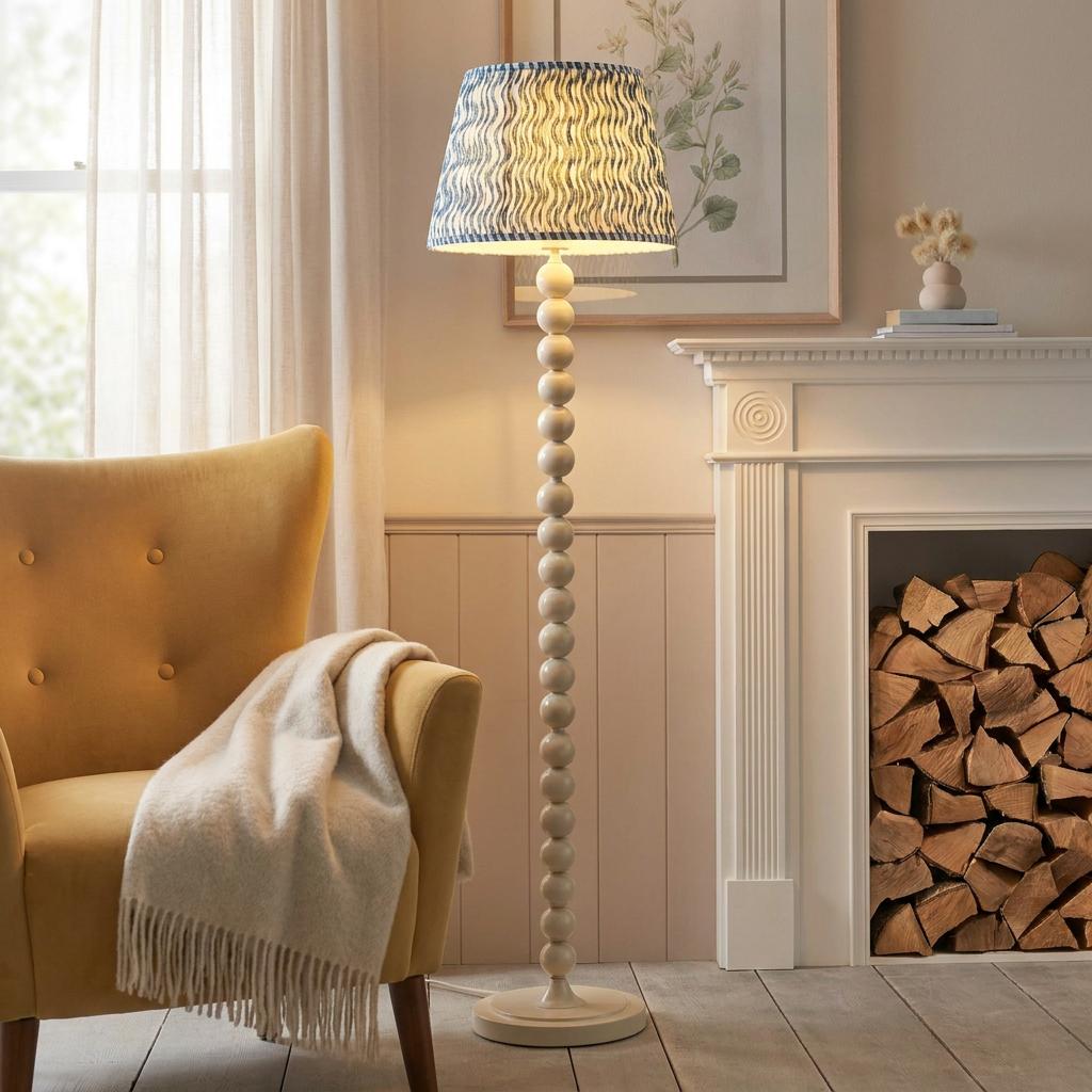 An almond white bobbin floor lamp with a blue rippled shade stands between a yellow armchair and a fireplace.