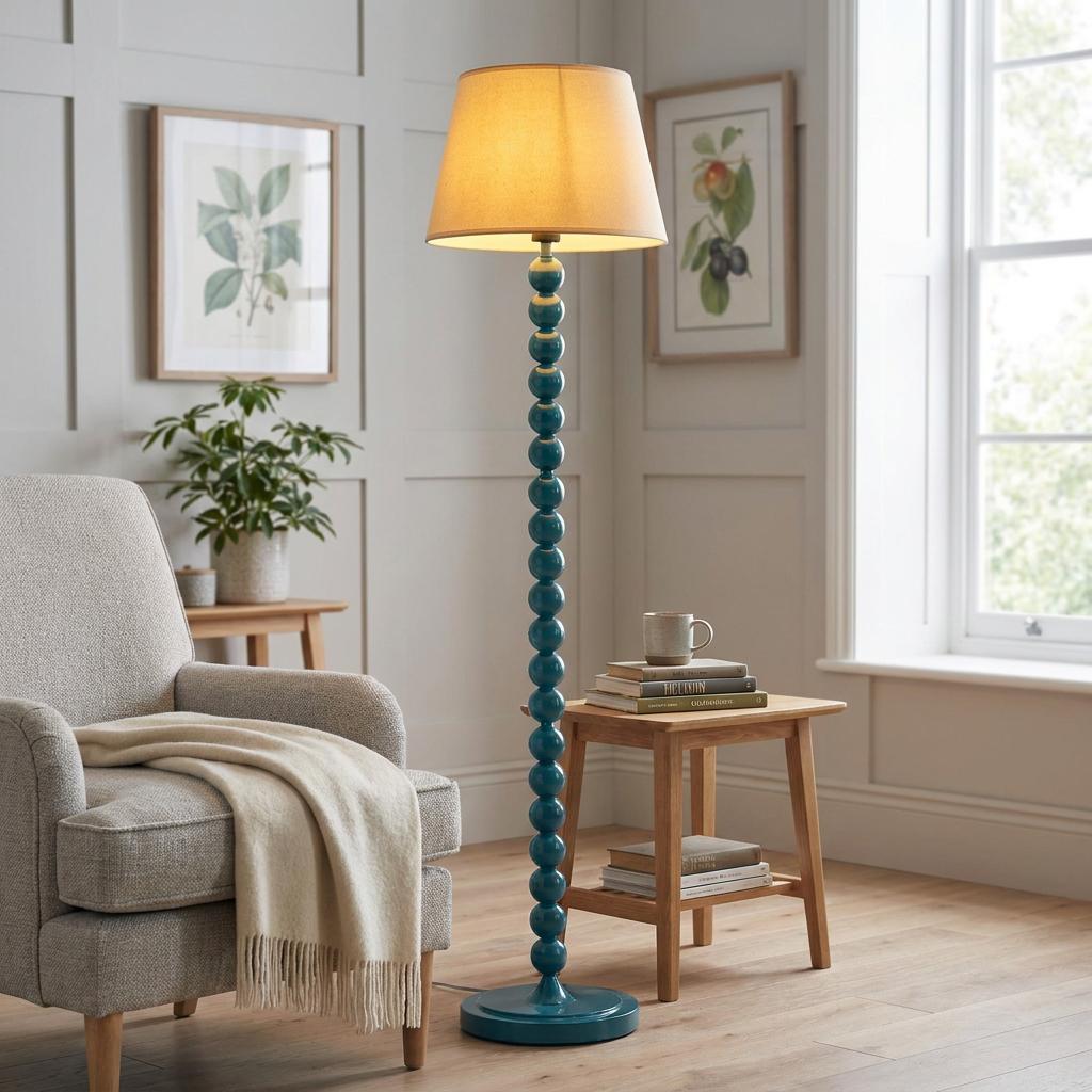 Teal beaded floor lamp with a lit neutral shade in a bright living room next to a grey armchair.