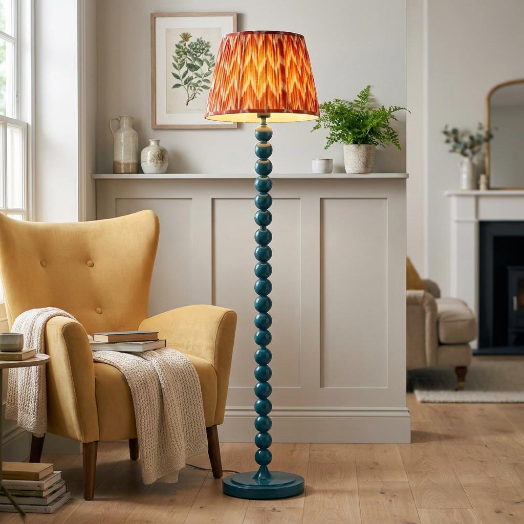 Teal bobbin floor lamp with an orange zigzag shade stands beside a yellow armchair in a bright living room.