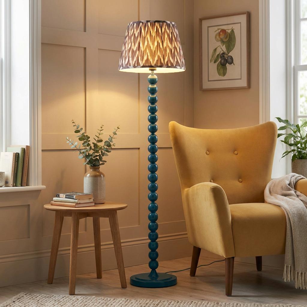 Teal blue bobbin floor lamp with a zigzag shade stands next to a yellow armchair in a warm living room.