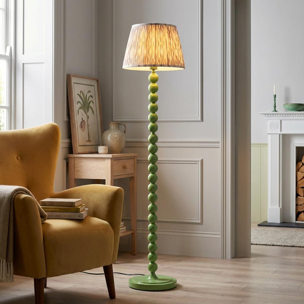Green bobbin floor lamp with a neutral ikat shade standing next to a yellow armchair in a bright living room.