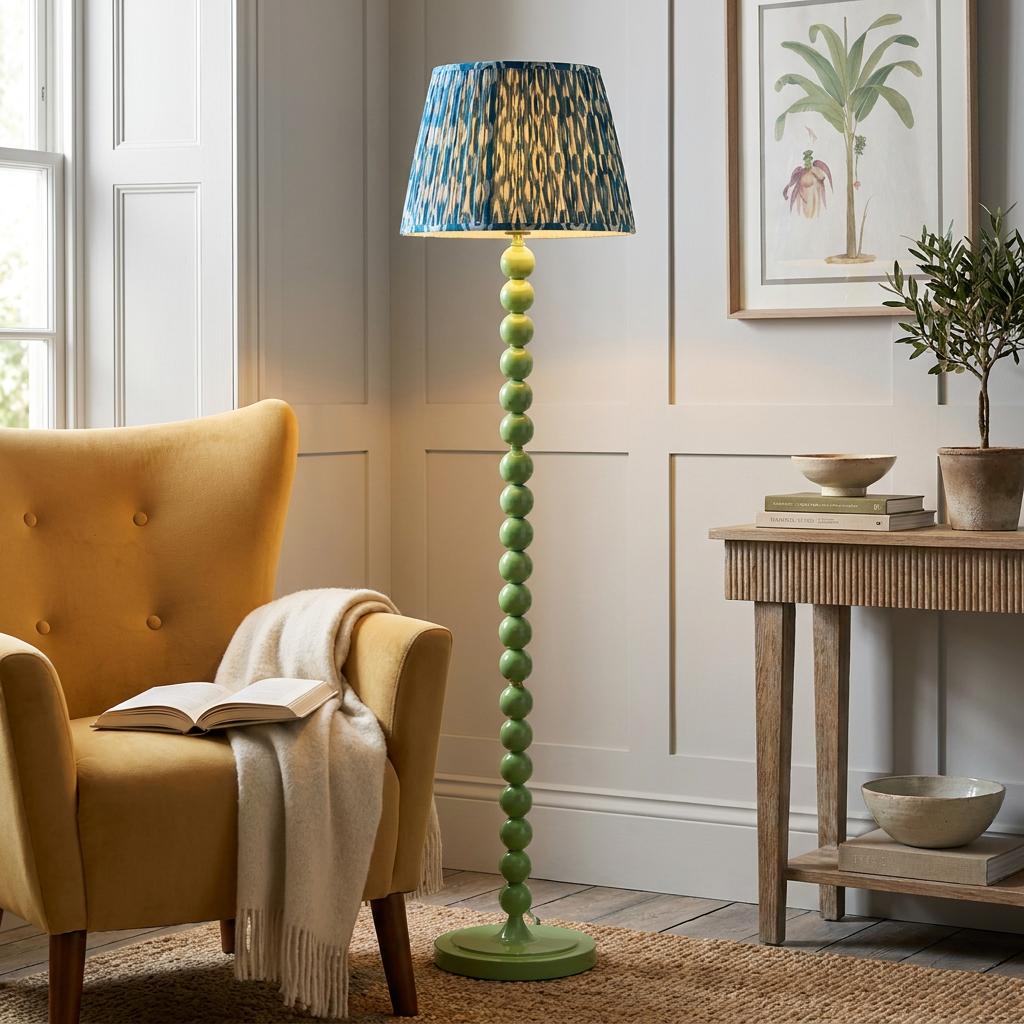 A green bobbin floor lamp with a blue ikat shade stands next to a yellow armchair in a cozy living room.