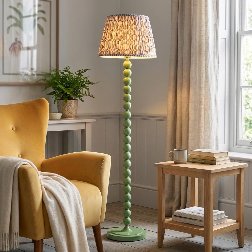 Green beaded floor lamp with a wavy patterned shade standing in a cozy living room next to a yellow armchair.