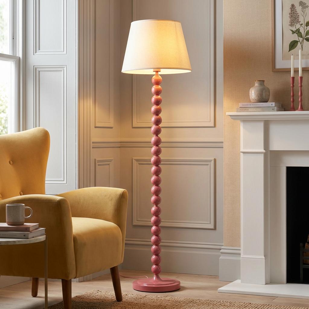 Pink bobbin floor lamp with a white shade standing beside a yellow armchair in a classic living room.