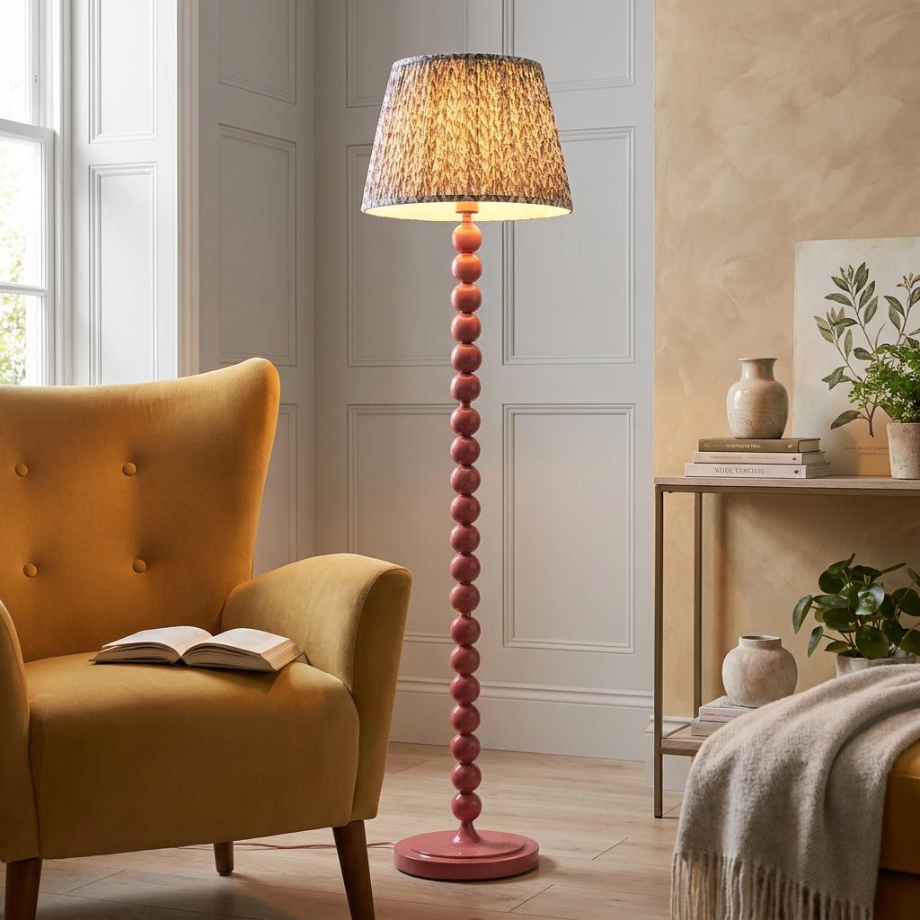 Pink floor lamp with beaded stem and leaf pattern shade next to a yellow velvet armchair in a lit living room.