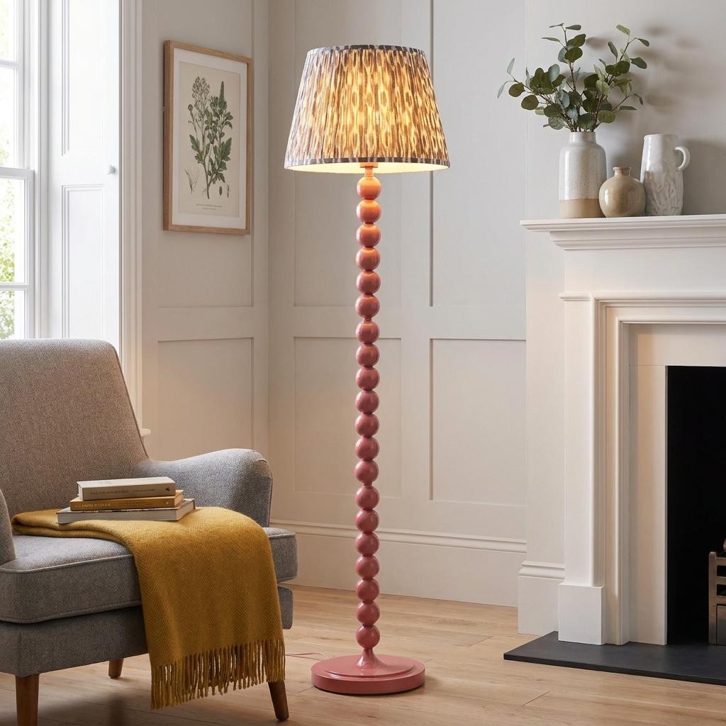 Higgledy pink floor lamp with a grey ikat shade in a living room with a grey armchair and a white fireplace.