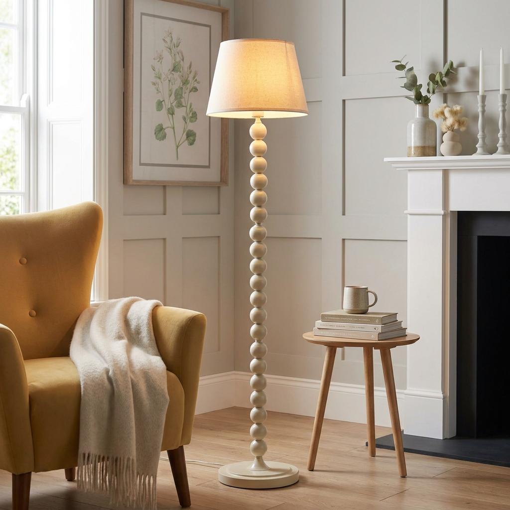 White floor lamp with a stacked-bead base and cream shade in a living room next to a yellow armchair.