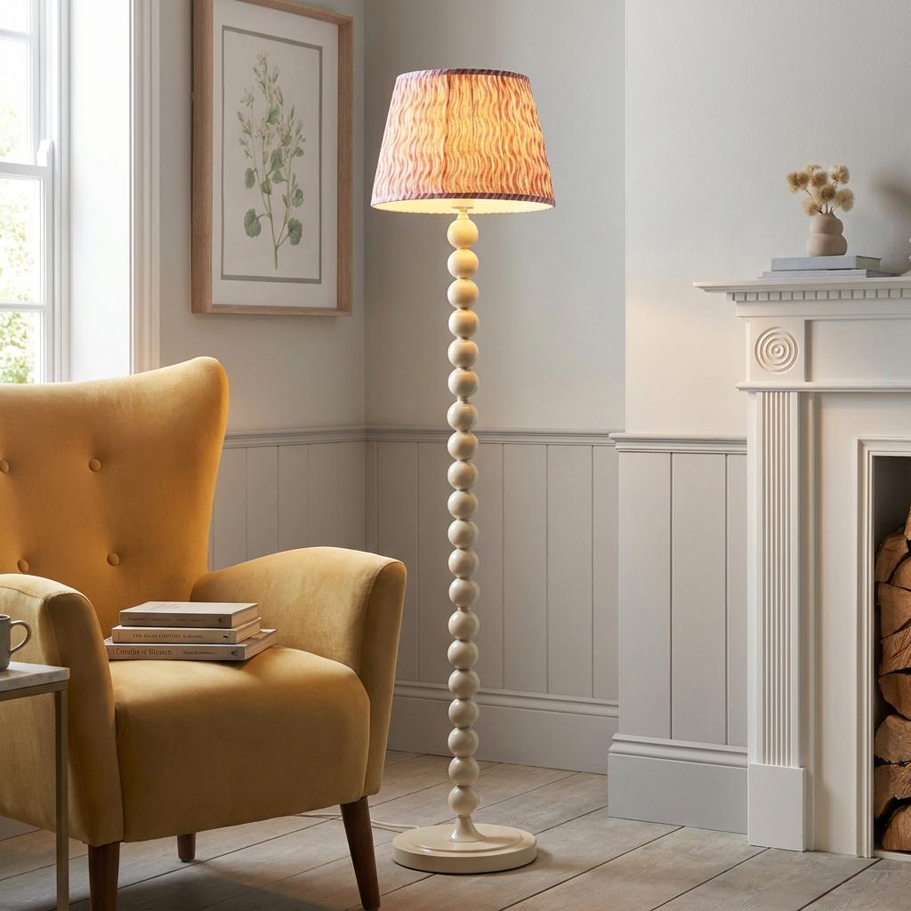 White bobbin floor lamp with a coral pink patterned shade standing in a living room next to a yellow armchair.