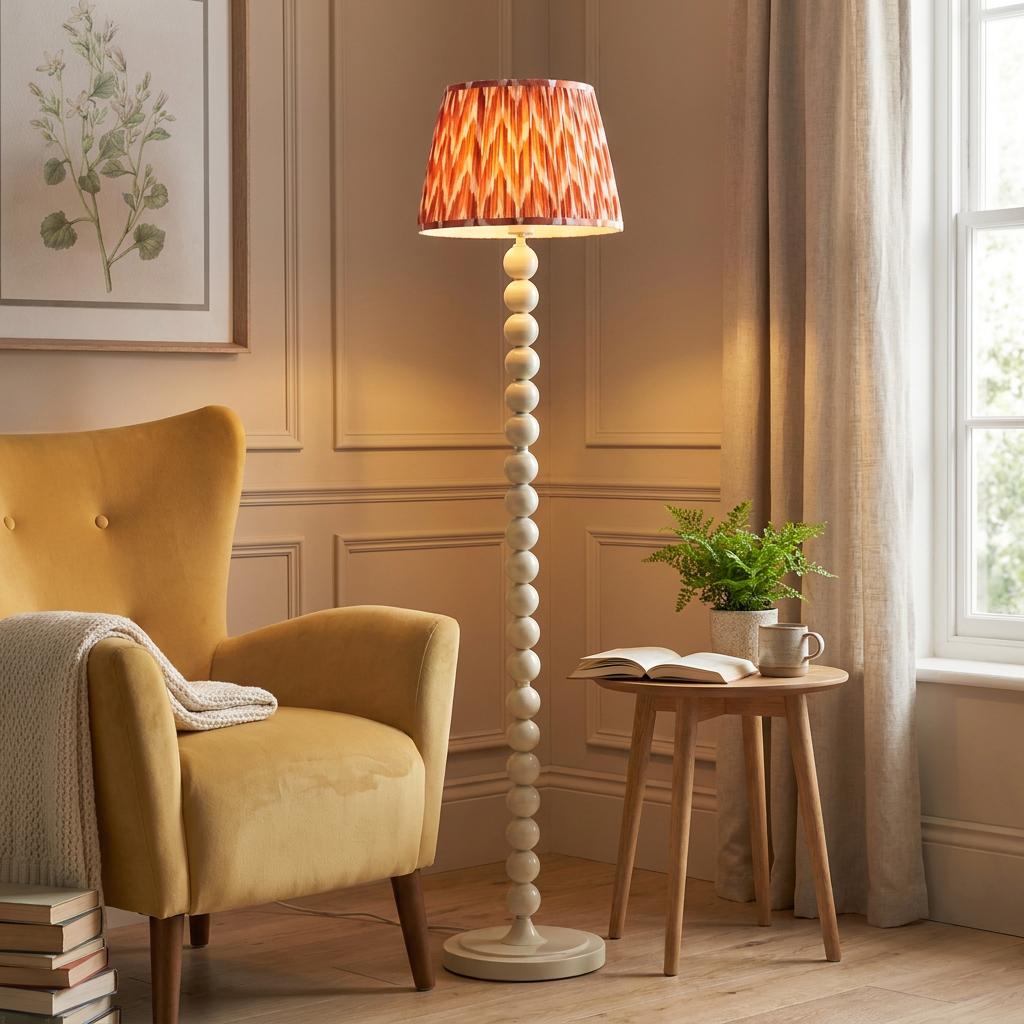 White bobbin floor lamp with an orange zigzag shade next to a yellow armchair in a warm living room.