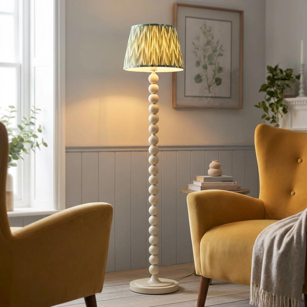A white bobbin floor lamp with a green zigzag shade stands between yellow armchairs in a cozy living room.