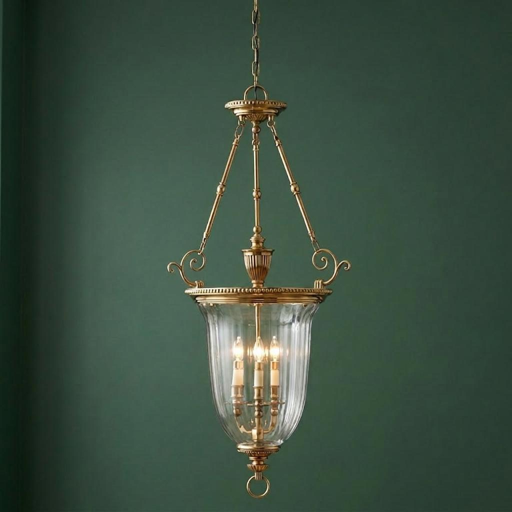 Hinkley Cambridge solid brass ceiling lantern with three candle lights and a clear bell glass shade against a green wall.