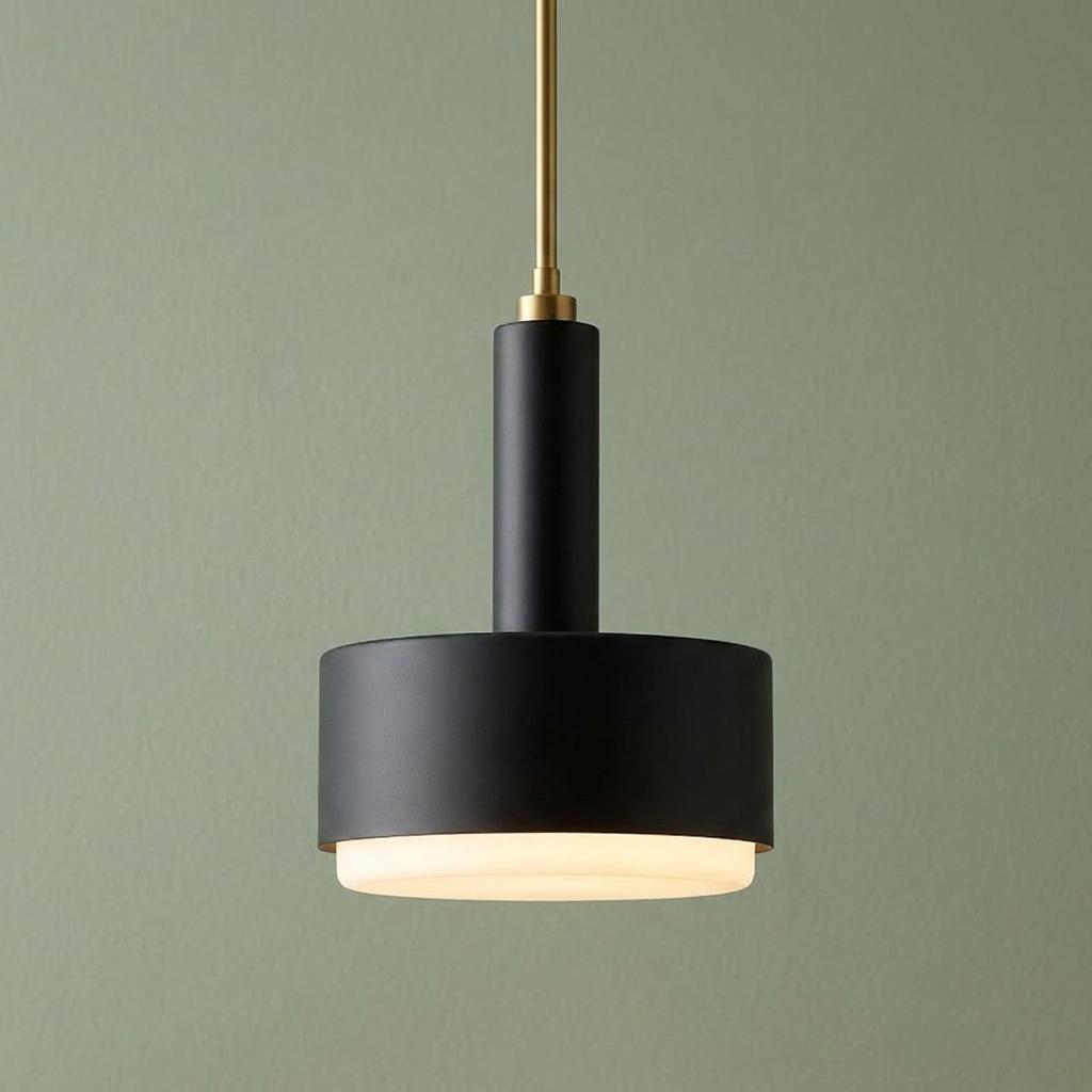 Modern black ceiling light with brass stem and glowing frosted diffuser against a sage green wall.