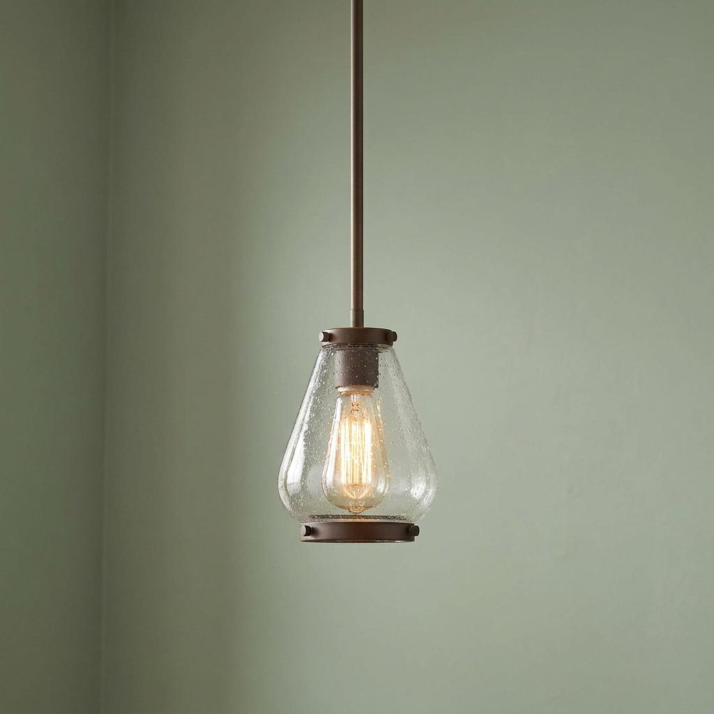 Mini bronze pendant light with a tapered seeded glass shade and Edison bulb against a sage green wall.