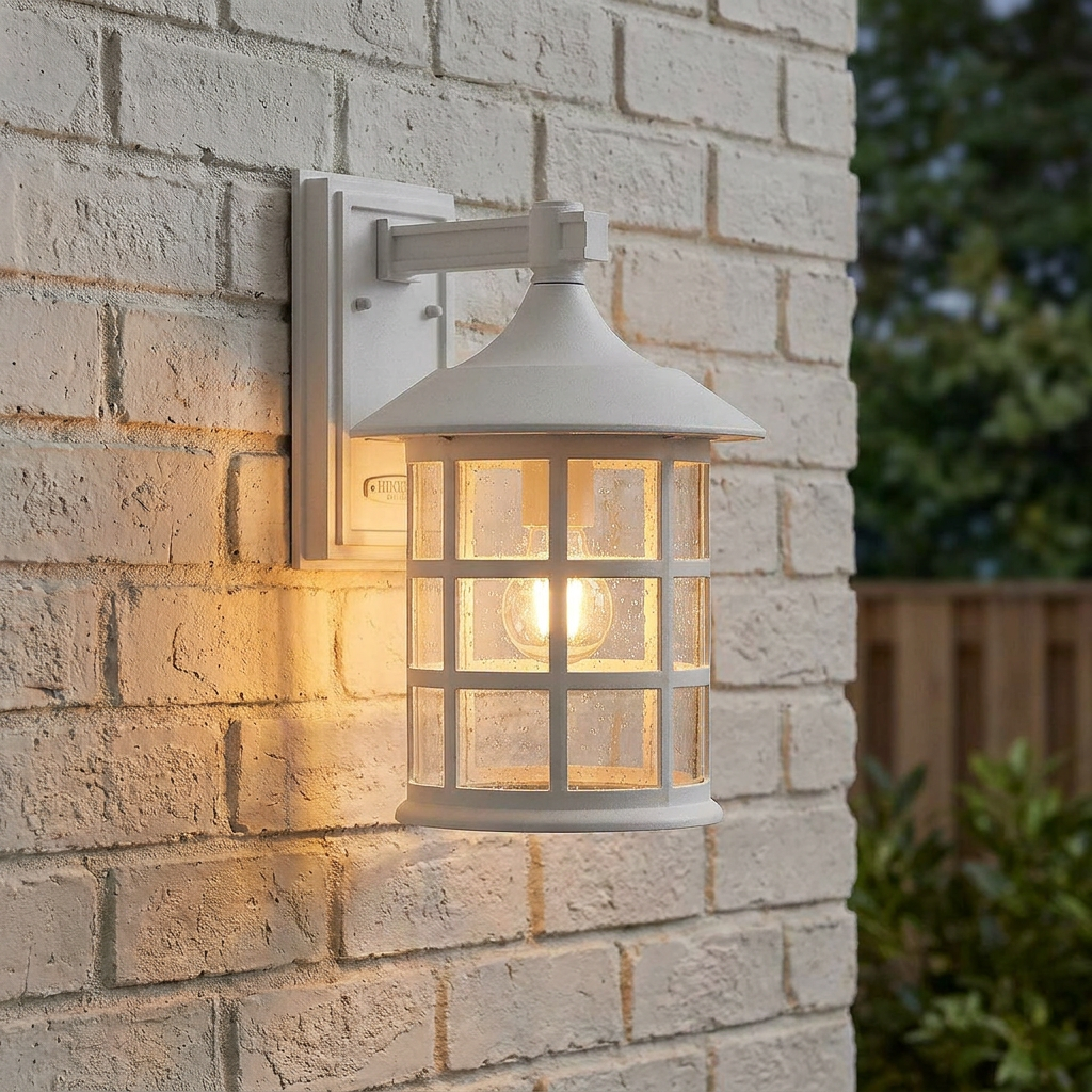 White lantern outdoor wall light with a lit bulb and grid cage, mounted on a light-colored brick wall.