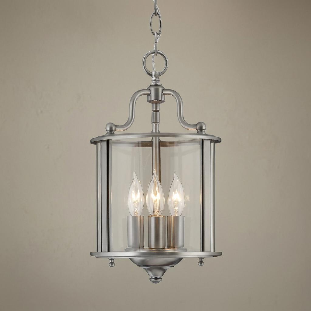 Classic pewter three-light ceiling lantern with curved clear glass panels and lit candelabra bulbs.
