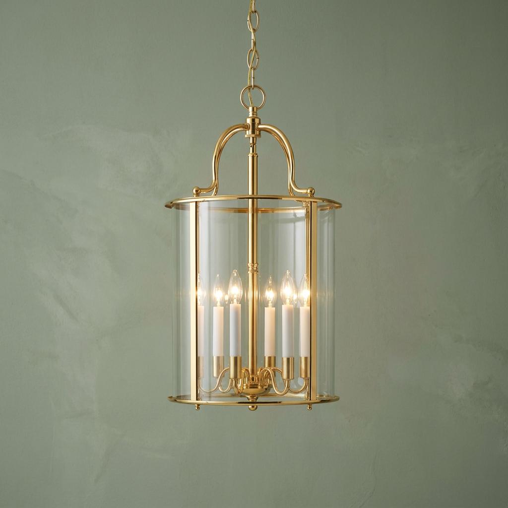 Polished brass 6-light lantern with clear glass panels and candle bulbs hanging against a sage green wall.