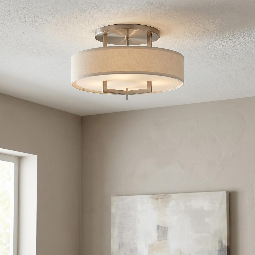 Brushed nickel semi-flush ceiling light with a linen drum shade, mounted on a white ceiling in a neutral room.