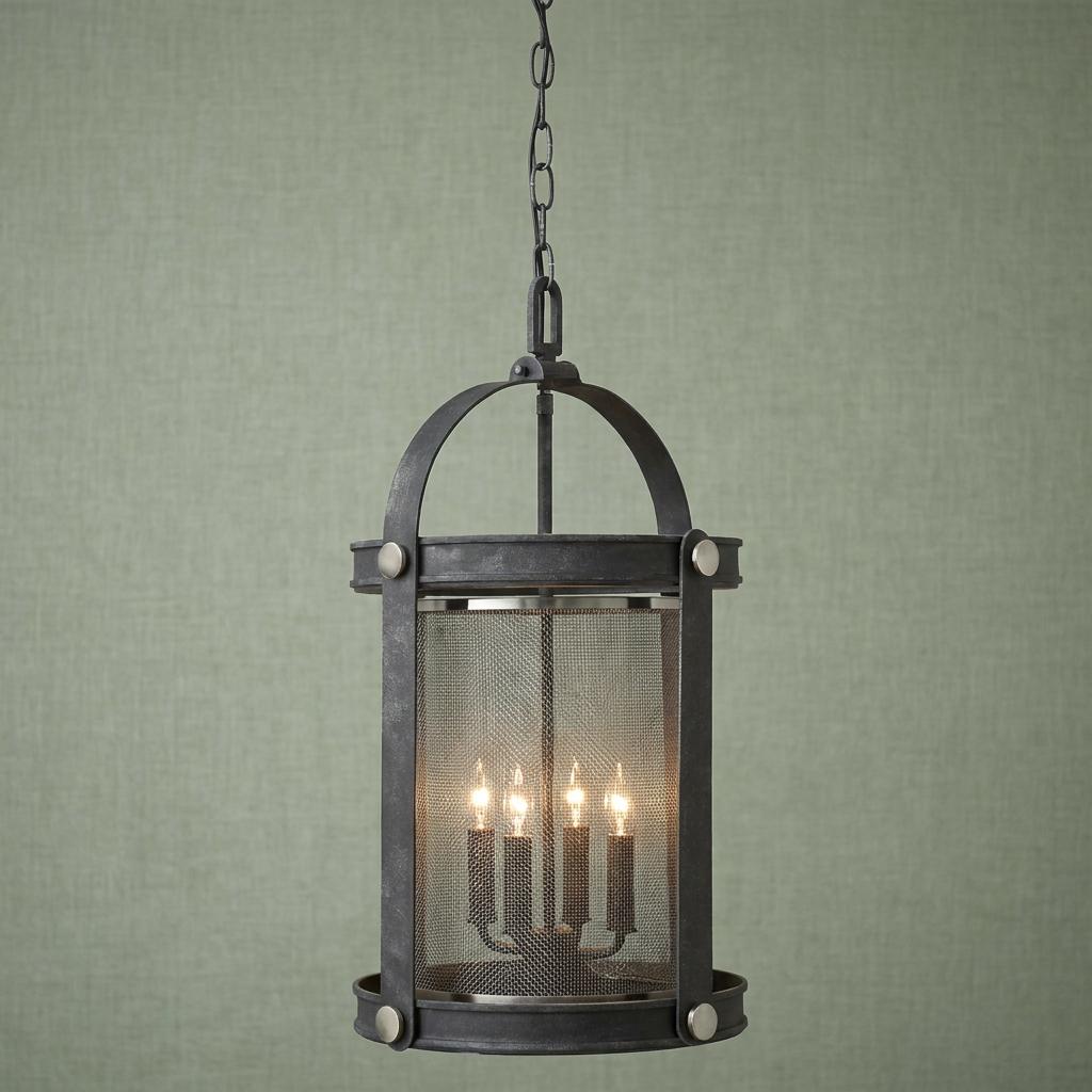Industrial zinc hanging lantern with four lit bulbs and a mesh screen against a textured green wall.