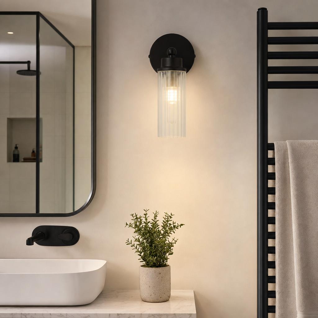 A matte black wall light with a clear ribbed glass shade mounted above a bathroom sink next to a mirror.