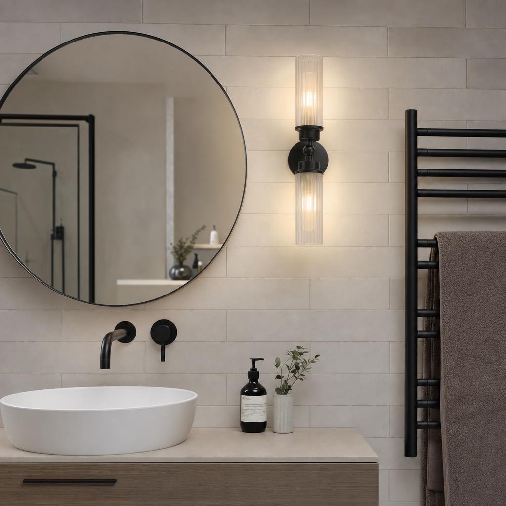 A black Imperial Bathroom wall light with fluted glass cylinders mounted beside a round mirror in a modern bathroom.