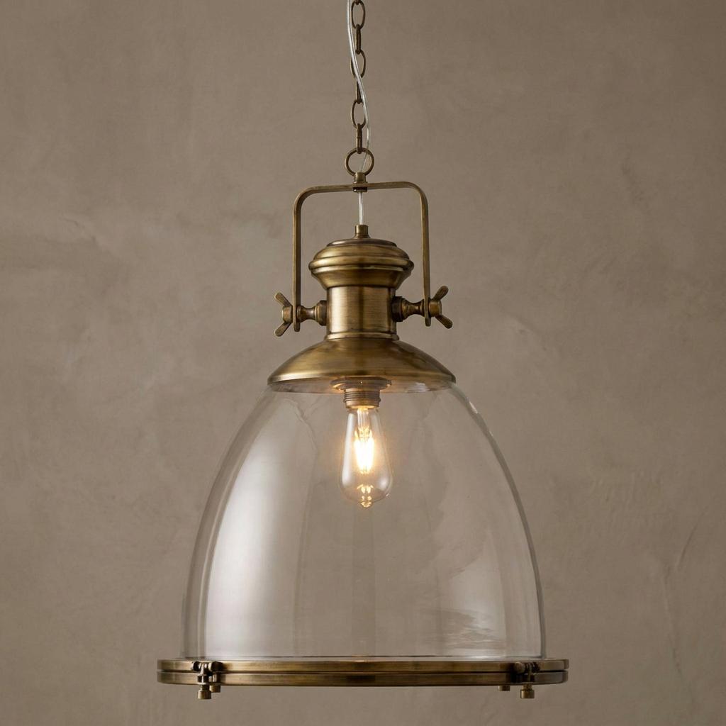 Industrial large brass and clear glass bell-shaped pendant light hanging against a neutral wall.