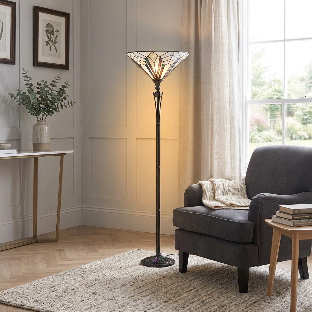 Art Deco Tiffany floor lamp with a stained glass shade glowing next to a grey armchair in a living room.