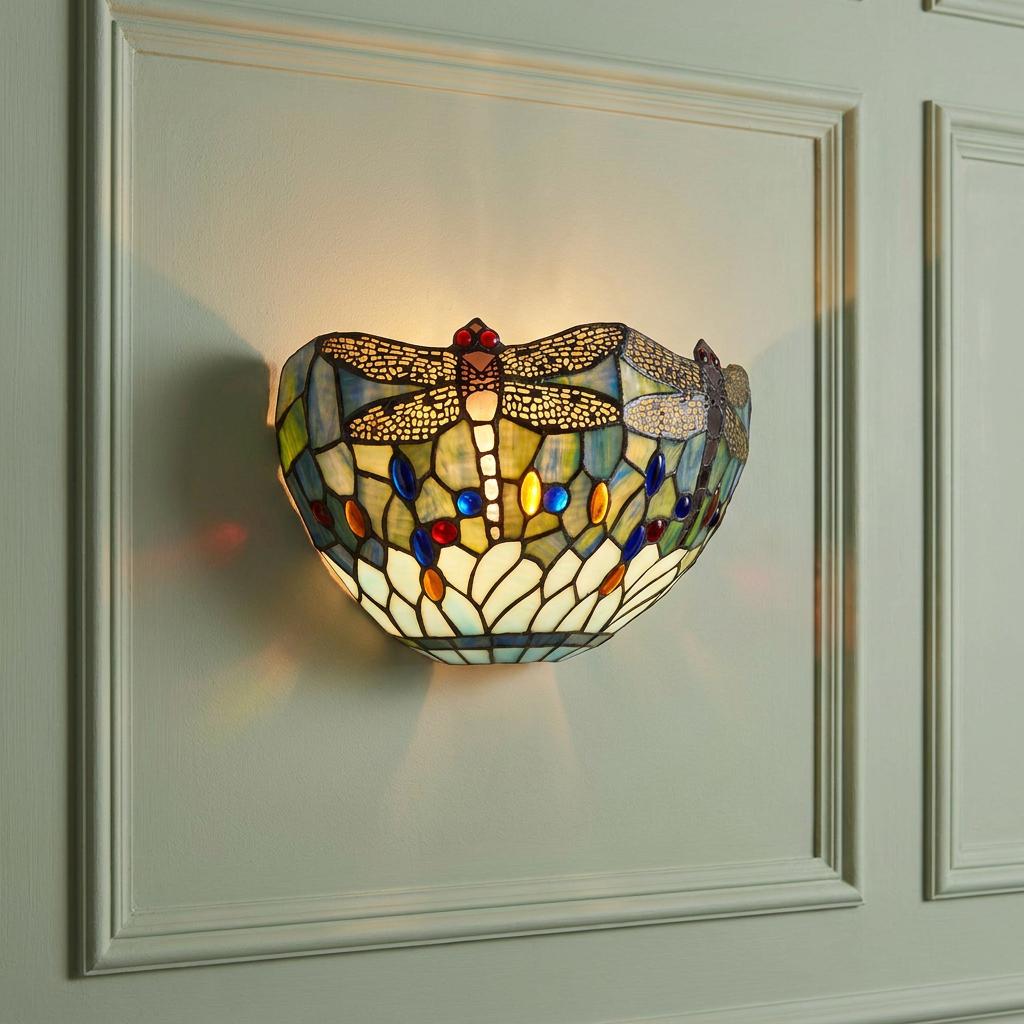 Blue dragonfly Tiffany-style stained glass wall light illuminated on a pale green panelled wall.