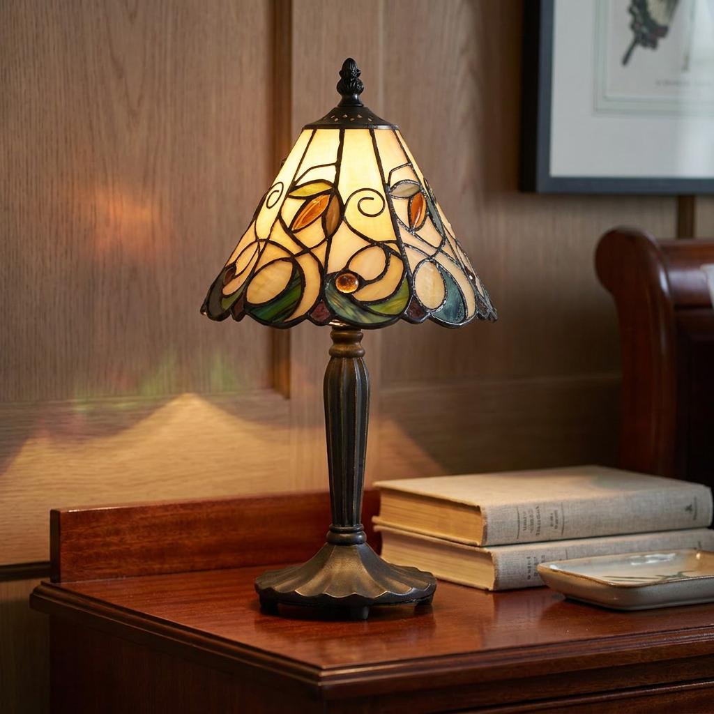 A glowing floral stained glass Tiffany lamp on a dark wood desk next to a stack of books.