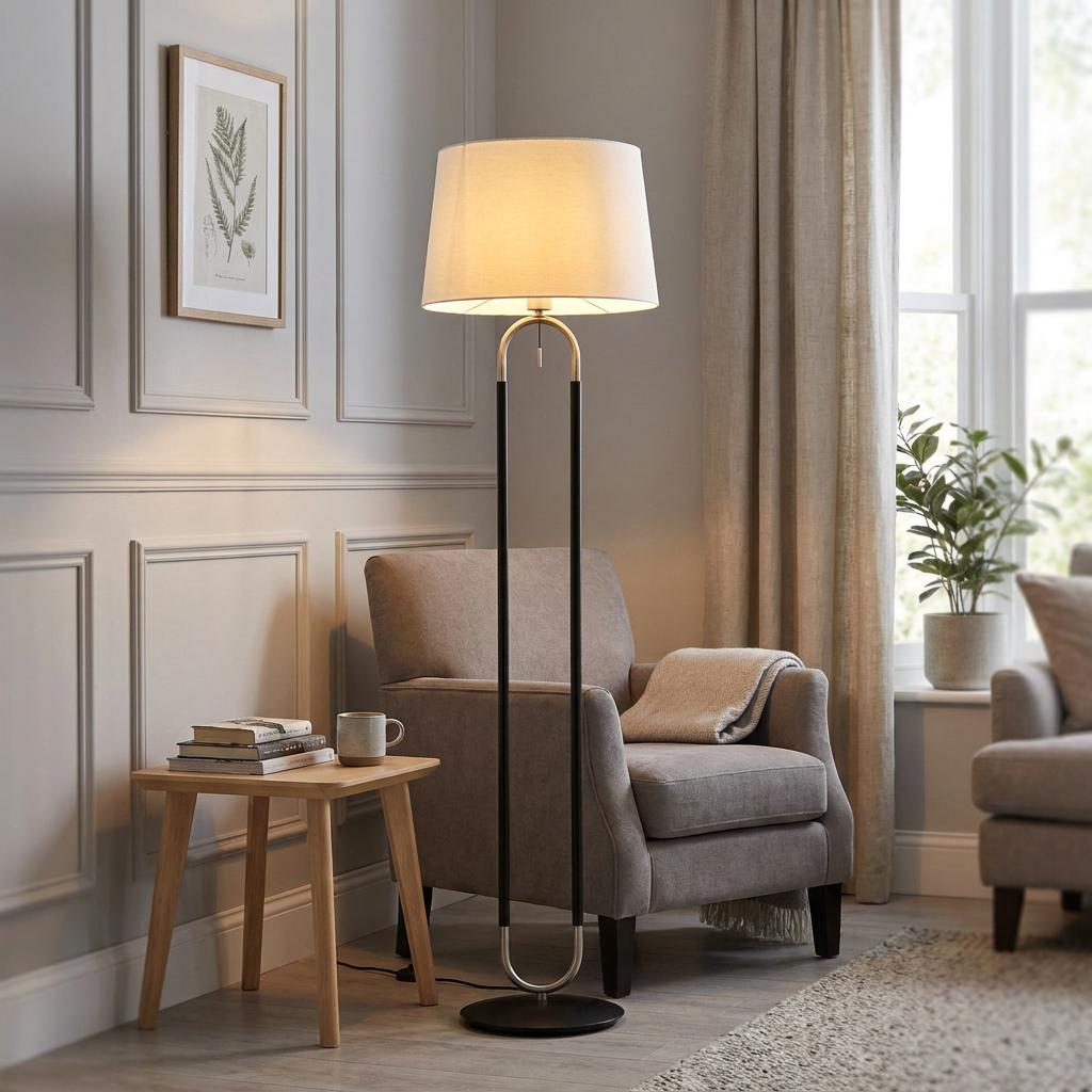 Jazz Silver & Black Floor Lamp with a cream shade standing beside a grey armchair in a modern panelled living room.