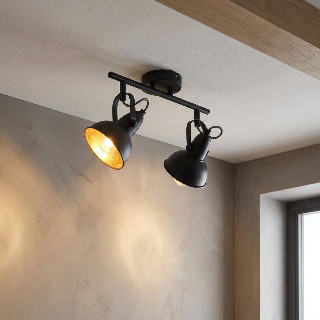 Jurva Urban black double bar spotlight with gold inner shades, mounted on a ceiling and illuminating a textured wall.
