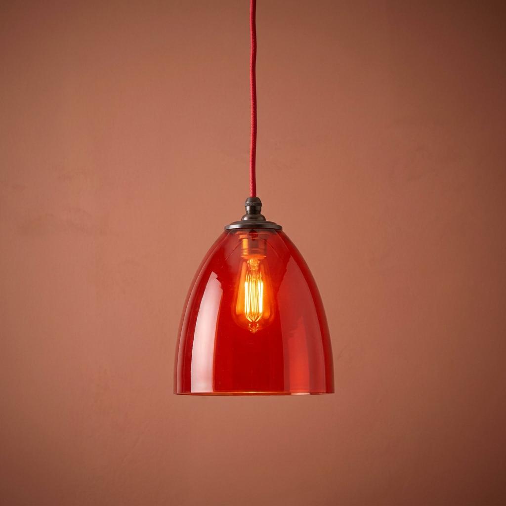 Burnt orange glass pendant light with a lit Edison bulb and red cord, set against a terracotta-colored wall.