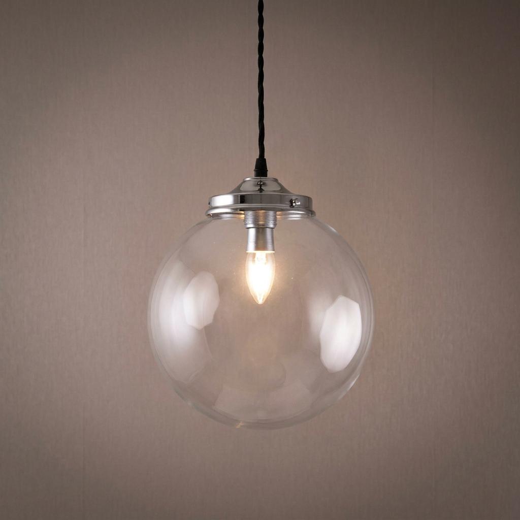 A lit clear glass globe pendant light with a polished chrome cap hanging against a neutral background.