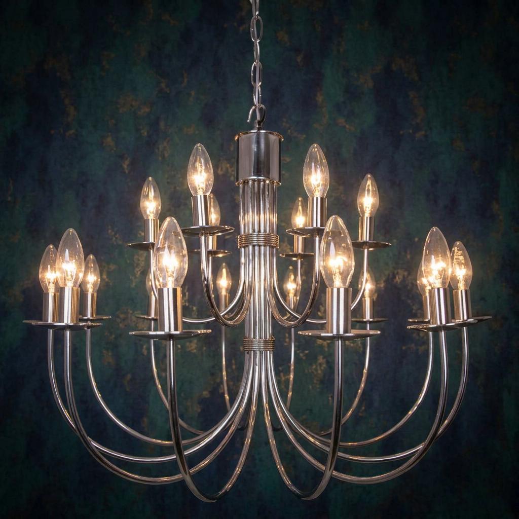 18-light stainless steel tiered chandelier with glowing candle bulbs against a dark, textured wall.