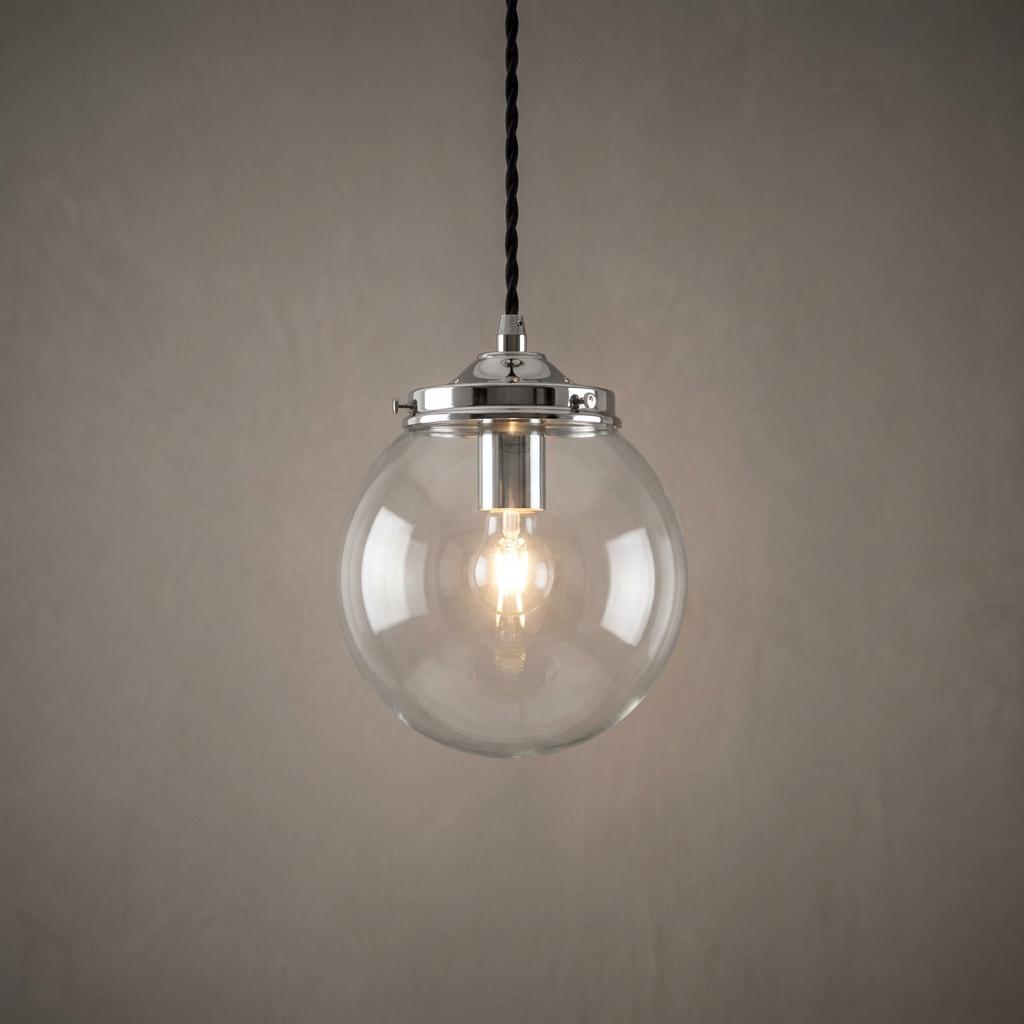 Illuminated clear glass globe pendant light with a chrome gallery and black twisted cord against a plain wall.