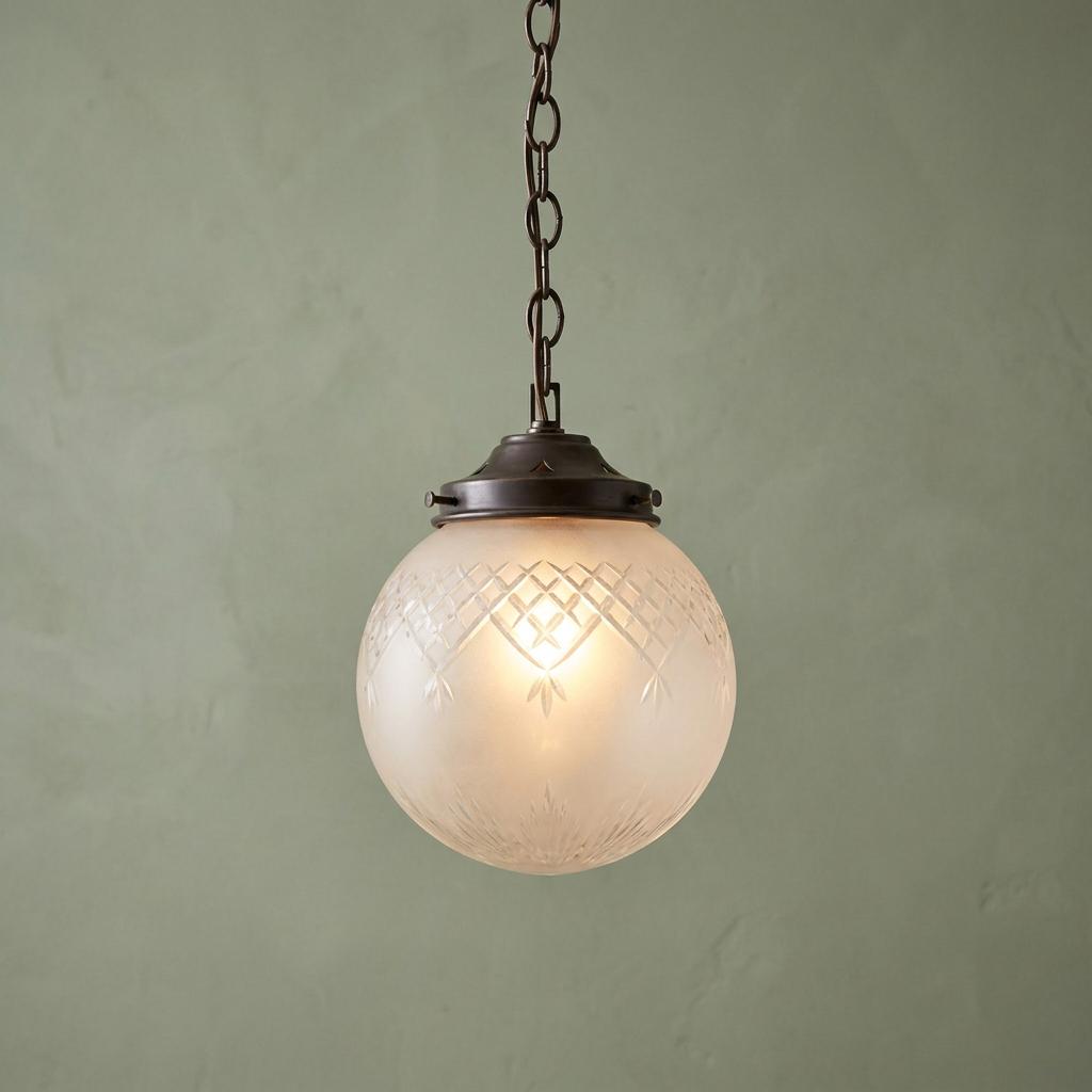 Art Deco ceiling light with an etched frosted glass globe and bronze chain against a sage green wall.