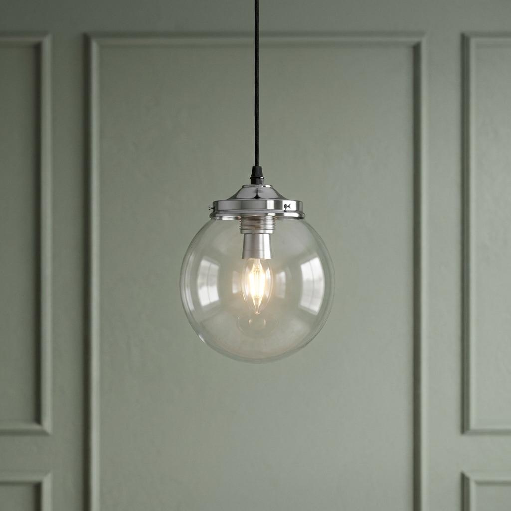 A Kansa clear globe pendant light with polished chrome hardware hangs against a sage green paneled wall.
