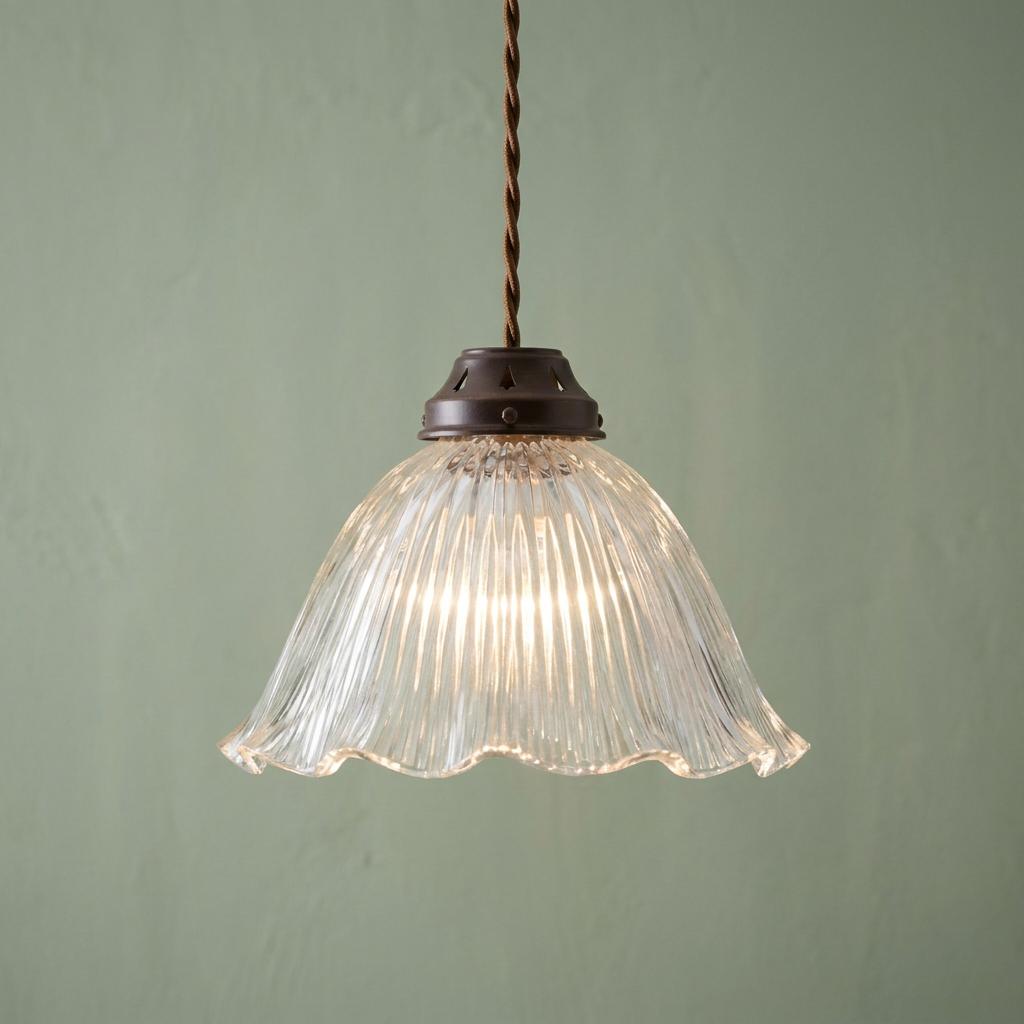 Ribbed glass pendant light with a frilled edge and bronze gallery hanging against a pale green wall.