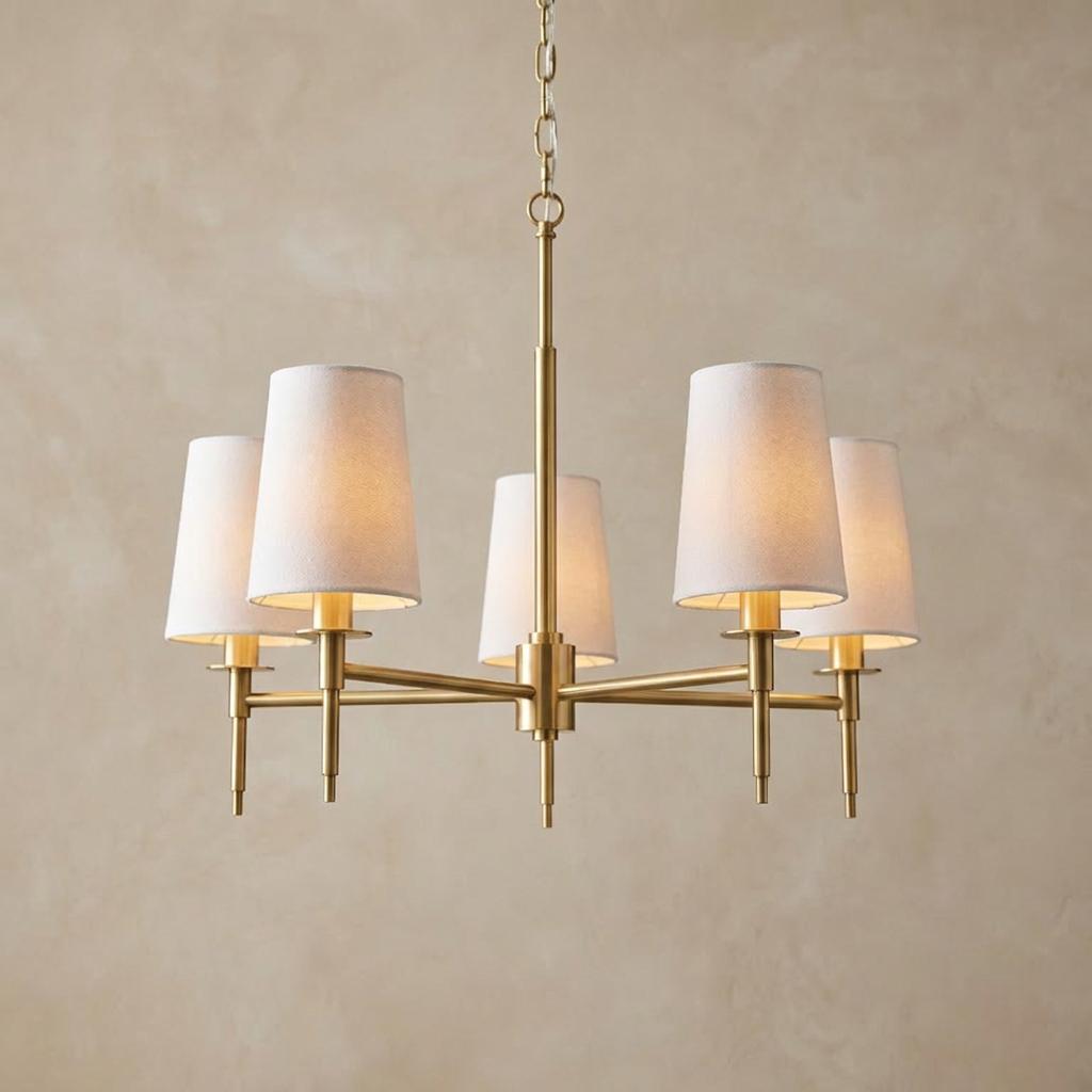 Kensington 5-light brass pendant with white tapered shades against a beige textured wall.