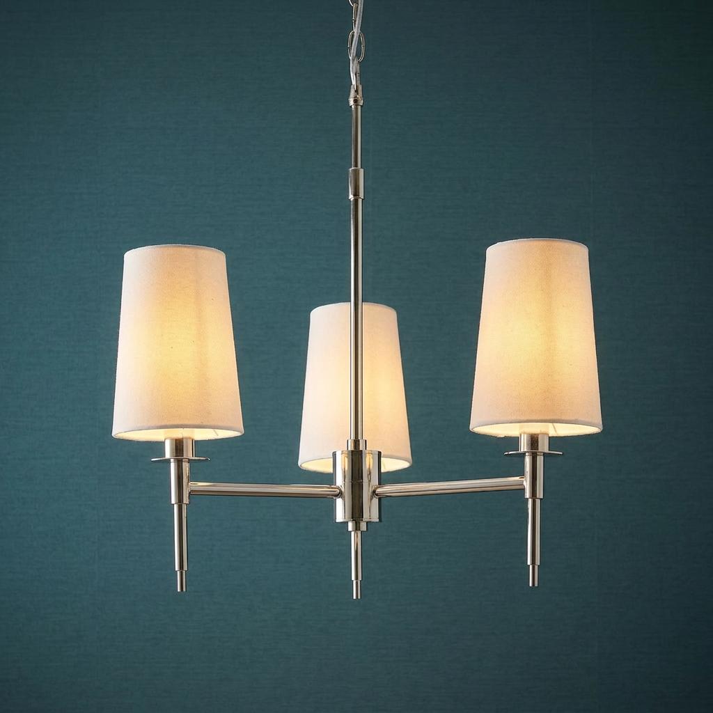 Three-light Art Deco pendant in polished nickel with glowing white shades against a teal blue wall.