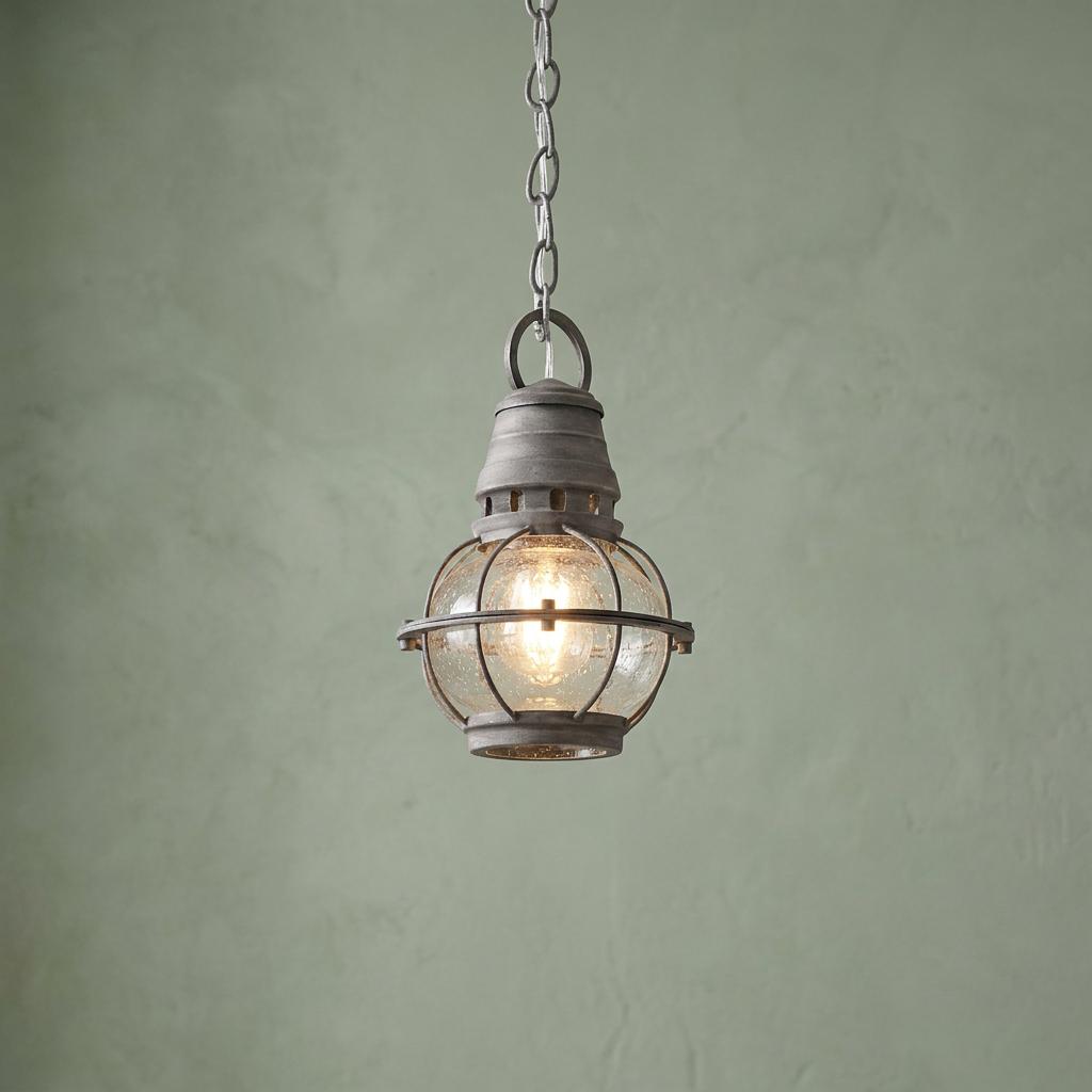 Nautical weathered zinc pendant light with a seeded glass globe hanging against a textured sage green wall.