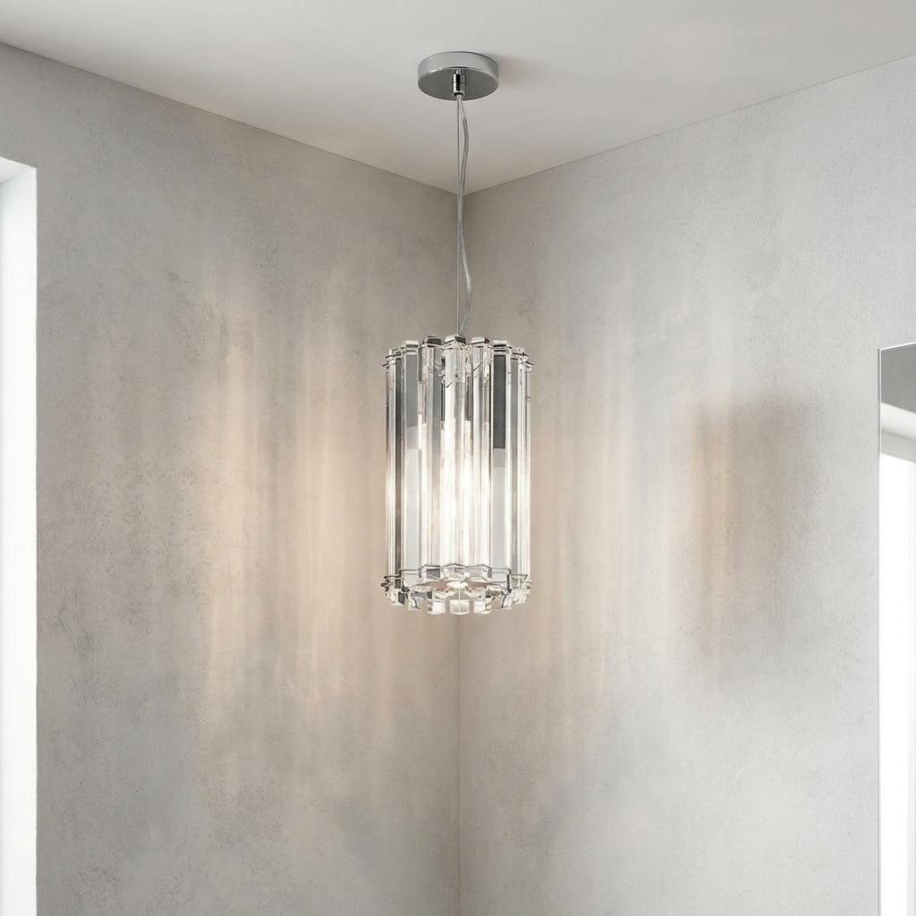 A cylindrical chrome pendant light with clear crystal prisms hanging in a room corner, casting a warm glow.