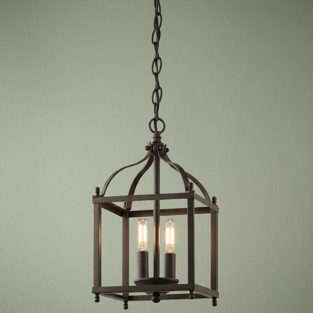 Olde Bronze 2-light pendant lantern with an open square frame and lit vintage bulbs against a green wall.
