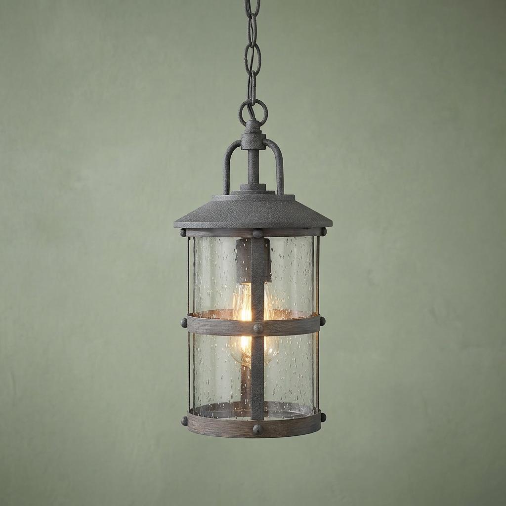 Rustic grey outdoor chain lantern with seeded glass and a lit bulb hanging against a green wall.