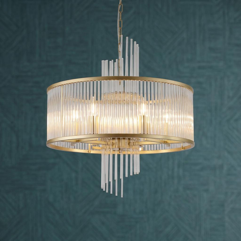 A gold pendant light with vertical clear glass rods illuminated against a textured teal wallpaper background.