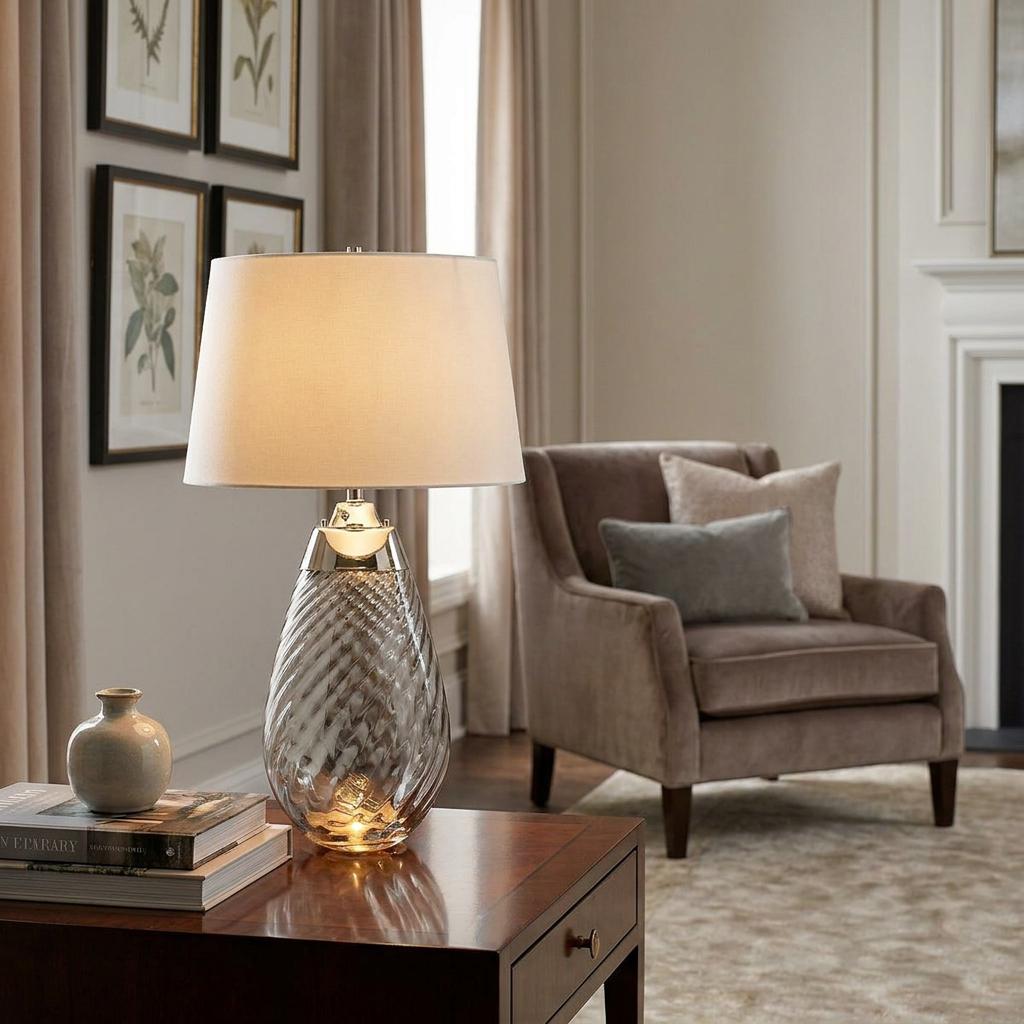 Lit smoke glass table lamp with an off-white shade on a wooden side table in a cozy living room.