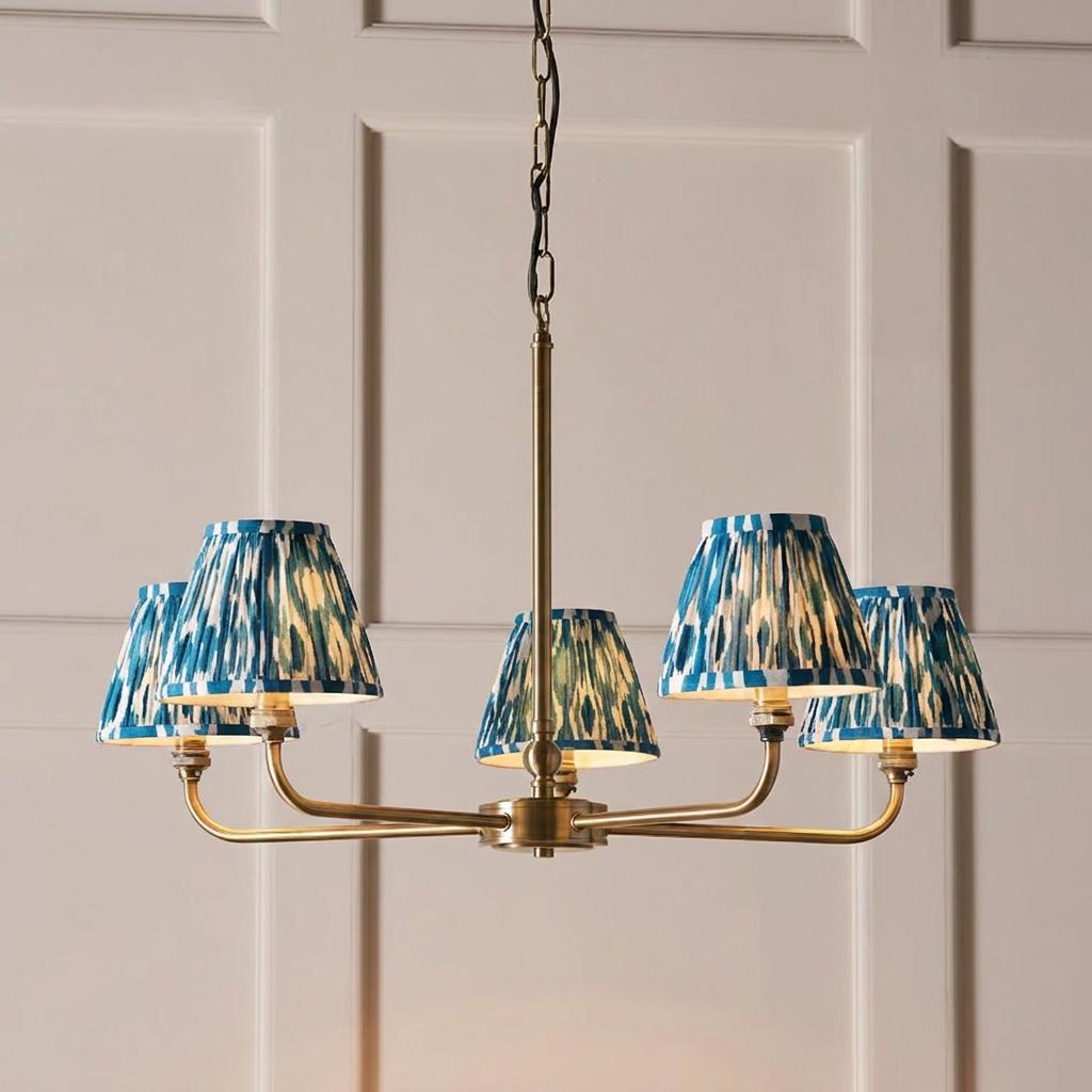 Brass 5-light chandelier featuring blue and white ikat patterned shades, hanging against a white paneled wall.