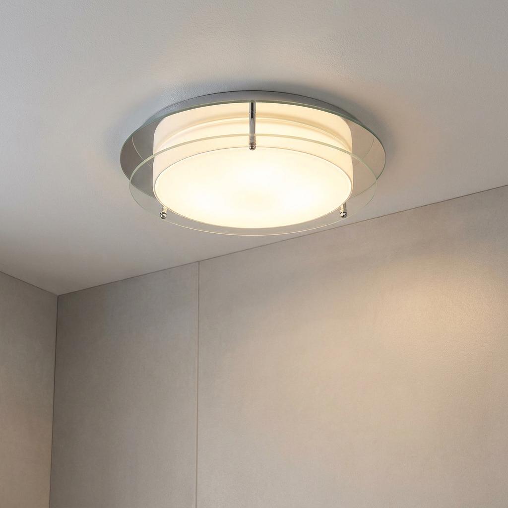 Circular flush ceiling light with opal and clear glass rings illuminated on a white bathroom ceiling.