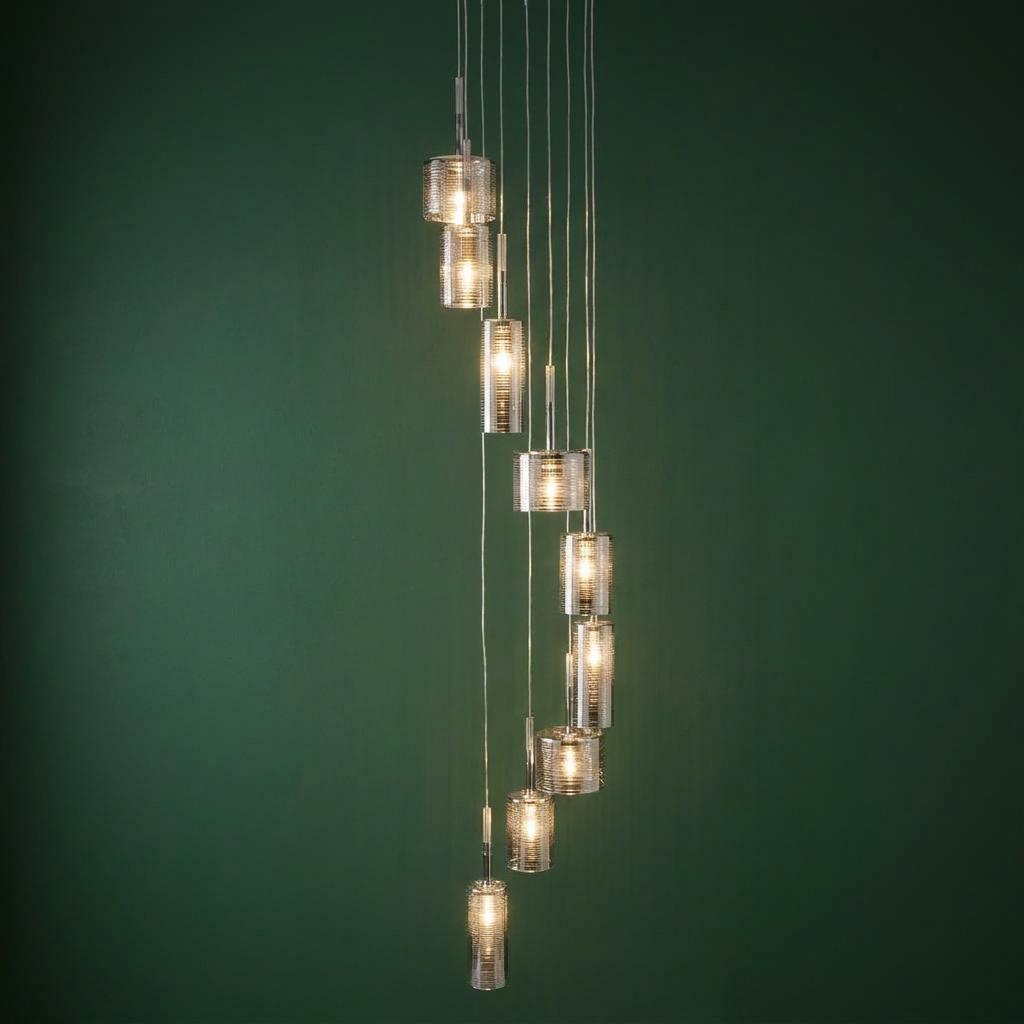 Linen 9 light multi-drop chrome pendant with cylindrical glass shades in a spiral arrangement against a green wall.
